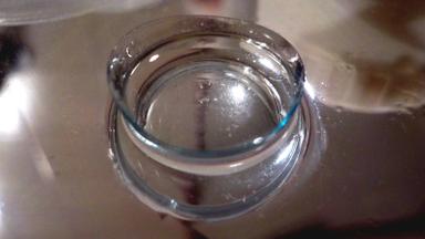 A clear soft contact lens resting in liquid on a reflective surface. Photo: Albarubescens via Wikimedia Commons, CC BY-SA 4.0 (cropped)