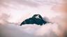 A dark mountain peak with a patch of snow rising above pink clouds. Photo: Cédric Servay via Wikimedia Commons, CC0 1.0 (cropped)
