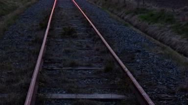 Railway tracks with rust-colored rails and gravel ballast at dusk. Photo: W.carter via Wikimedia Commons, CC0 1.0 (cropped)