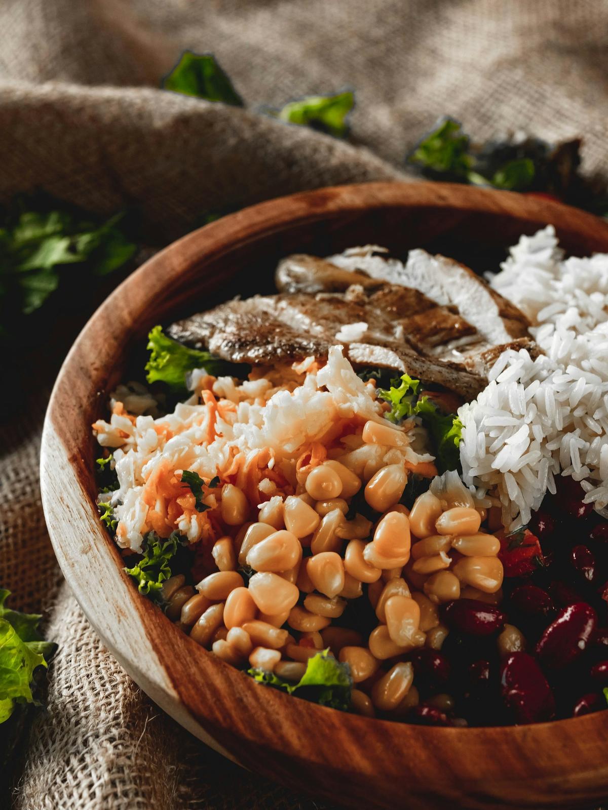 Wooden bowl of rice, kidney beans, corn and sliced chicken on burlap. Photo: Joe Boshra on Unsplash