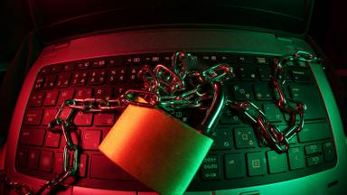 A padlock and chain resting on a laptop keyboard under red and green light. Photo: FlyD on Unsplash