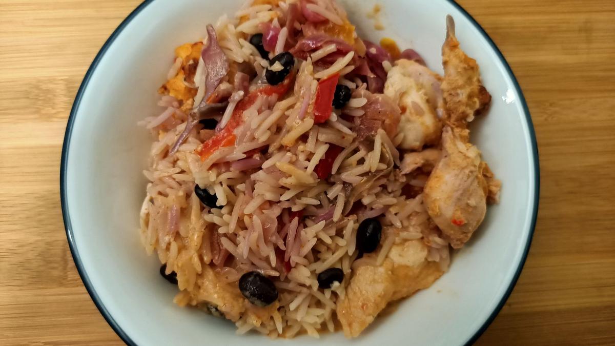 A bowl of rice, black beans, peppers and chicken on a wooden table. Photo: JaredMcKenzie via Wikimedia Commons, CC0