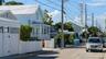 A quiet residential street in Key West, Florida, lined with pastel wooden houses, white picket fences and palm trees under a blue sky. Photo: Residential Street in Key West, Florida, Julian Lupyan / Wikimedia Commons, CC0 (cropped and resized)