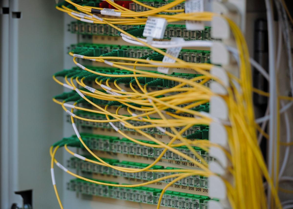 Close-up of yellow fiber optic cables plugged into a green network patch panel. Photo: Albert Stoynov on Unsplash
