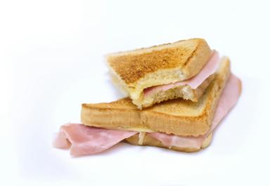 Two toasted ham sandwiches stacked on a plain white background, with a slice of ham hanging out of the lower sandwich. Photo: Glenn Diaz via Unsplash
