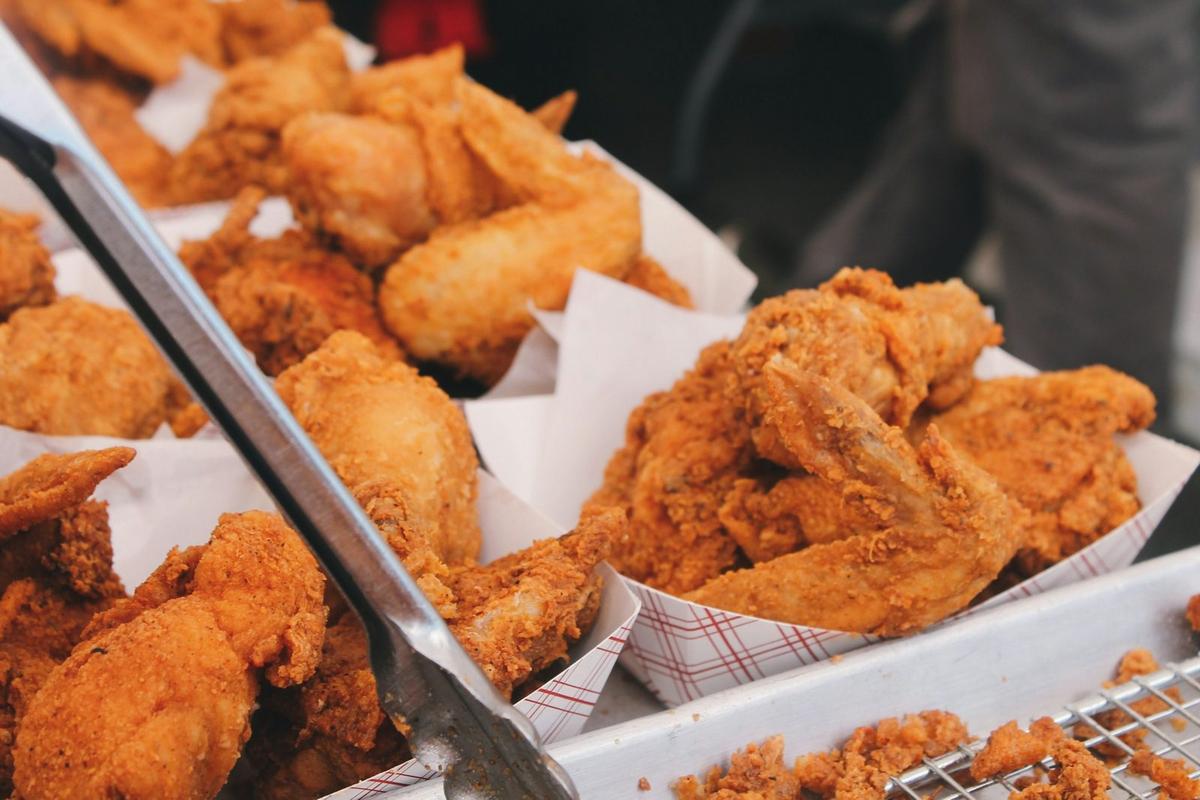 Fried chicken pieces on paper trays at a food stall, with tongs resting on the tray. Photo: Brian Chan on Unsplash.