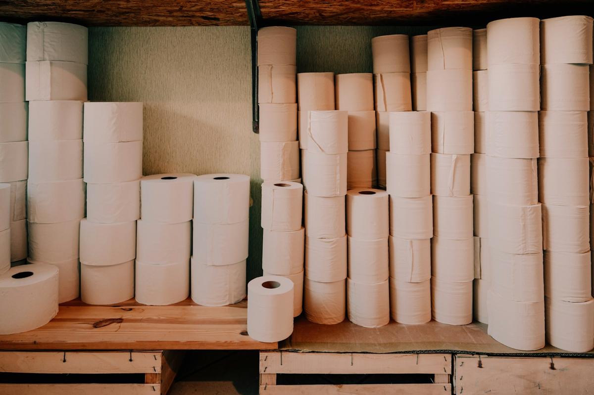 Stacks of white tissue rolls on wooden shelves and crates in a storeroom. Photo: Konstantin Volke on Unsplash.