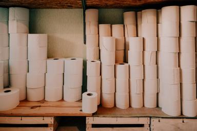 Stacks of white tissue rolls on wooden shelves and crates in a storeroom. Photo: Konstantin Volke on Unsplash.